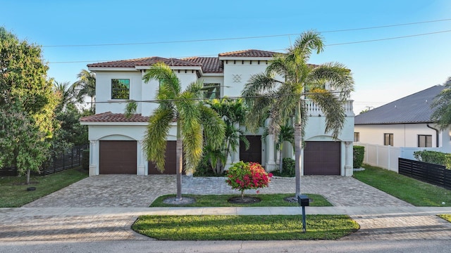 mediterranean / spanish-style house featuring stucco siding, decorative driveway, fence, and a tiled roof