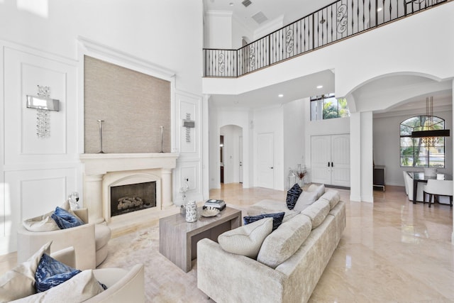 living room with a fireplace with raised hearth, arched walkways, ornamental molding, a towering ceiling, and marble finish floor