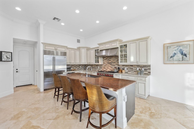 kitchen with visible vents, stainless steel built in refrigerator, under cabinet range hood, cream cabinetry, and a sink