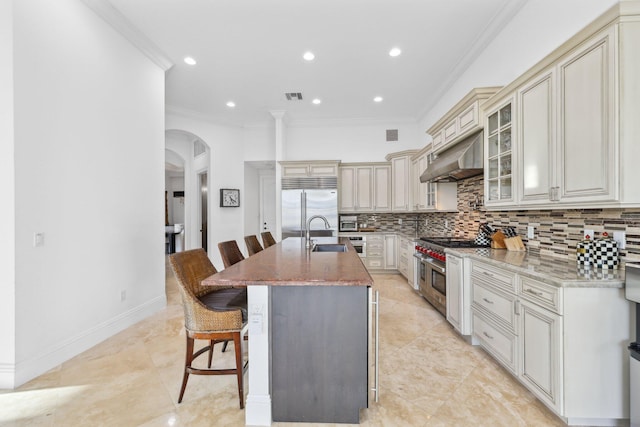 kitchen with visible vents, high quality appliances, a sink, backsplash, and arched walkways