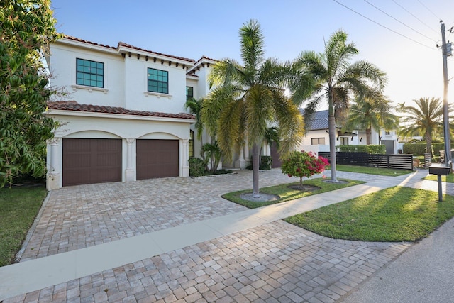 mediterranean / spanish-style home with stucco siding, a tile roof, decorative driveway, and fence