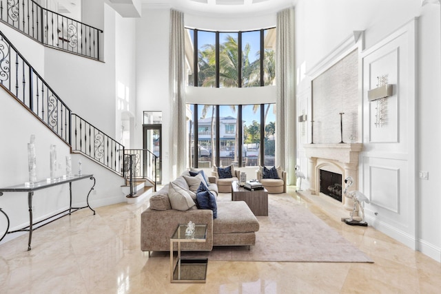 living room featuring marble finish floor, stairway, a premium fireplace, baseboards, and a towering ceiling