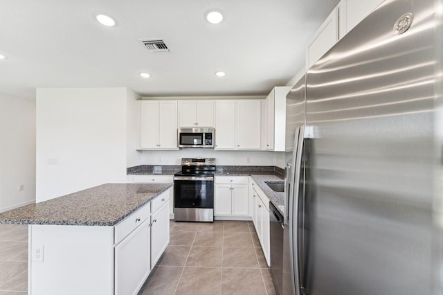 322 Becker Rd Unit 13, Port Saint Lucie, FL 34953 - kitchen featuring stainless steel appliances, light tile patterned flooring, dark stone counters, a center island, and white cabinets
