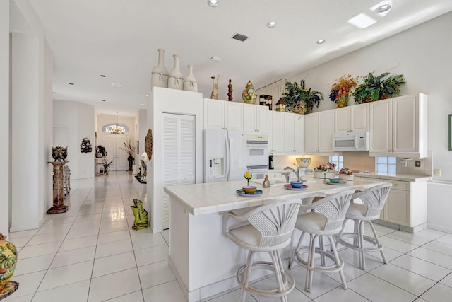 kitchen with light tile patterned floors, a kitchen island with sink, white appliances, and visible vents