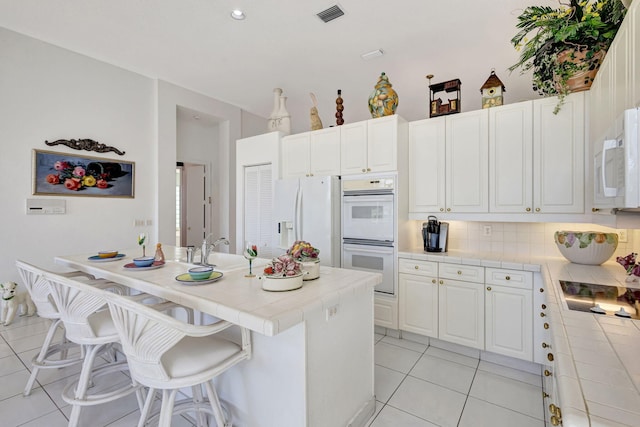 kitchen with tile countertops, a breakfast bar area, visible vents, white cabinetry, and white appliances