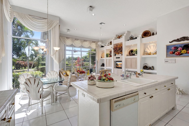 kitchen with light tile patterned floors, tile counters, white cabinets, white dishwasher, and a sink