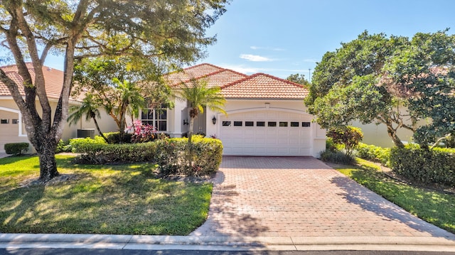 mediterranean / spanish home featuring a tile roof, an attached garage, decorative driveway, a front lawn, and stucco siding