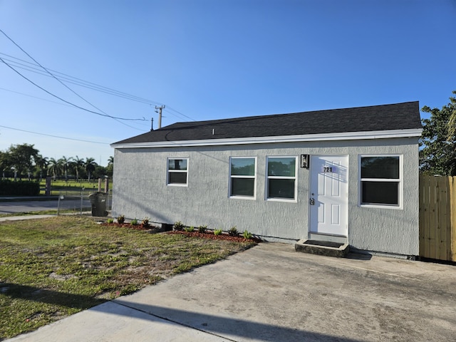 bungalow-style home with stucco siding, roof with shingles, and fence