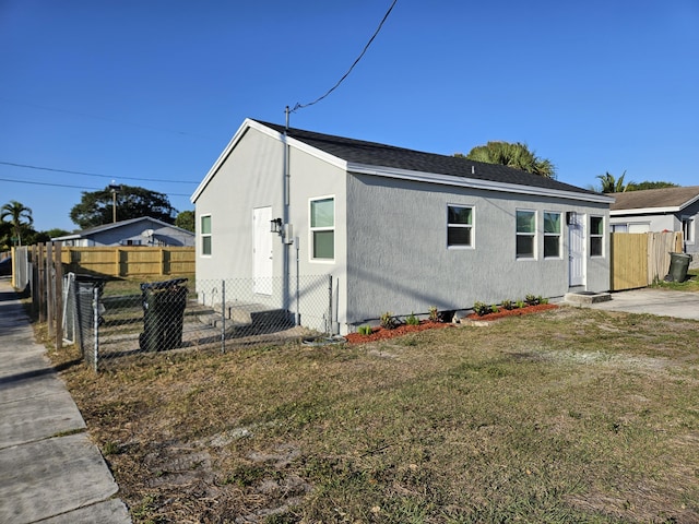 view of front of property featuring stucco siding, roof with shingles, a front lawn, and fence