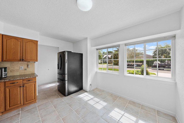 kitchen featuring baseboards, backsplash, stainless steel fridge with ice dispenser, dark stone counters, and brown cabinetry