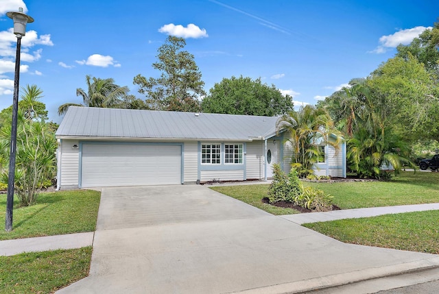 ranch-style house with metal roof, an attached garage, driveway, and a front yard