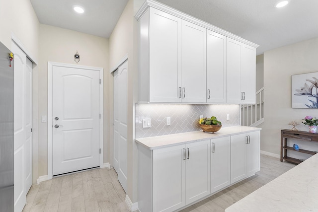 interior space with light wood-style flooring, recessed lighting, white cabinets, decorative backsplash, and baseboards