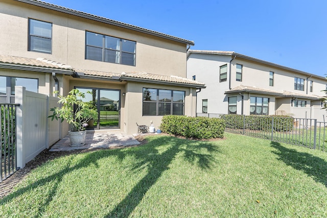 rear view of house featuring fence, a tile roof, stucco siding, a lawn, and a patio area