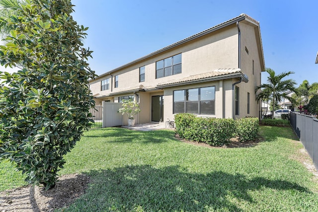 back of property with a tiled roof, fence private yard, a lawn, and stucco siding