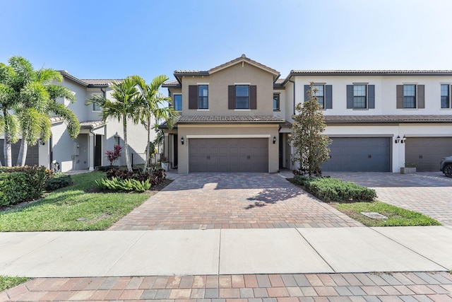 view of front of property with a tiled roof, decorative driveway, a garage, and stucco siding