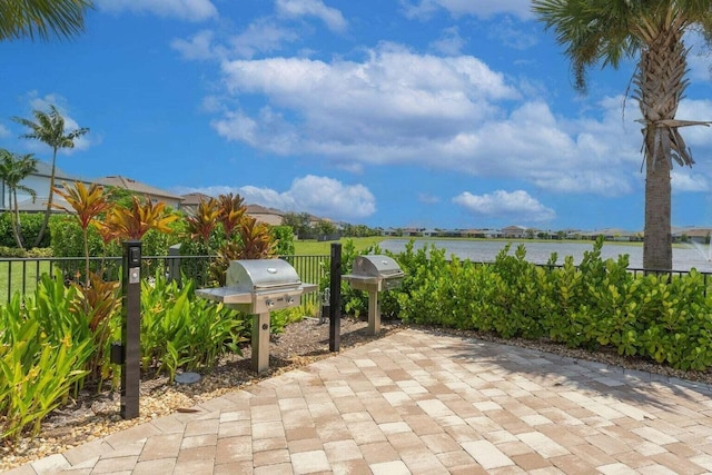 view of patio with a water view, a grill, and fence