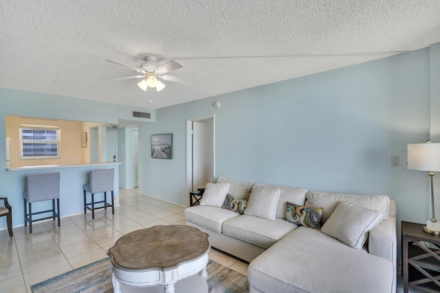 living area featuring light tile patterned floors, visible vents, a textured ceiling, and a ceiling fan