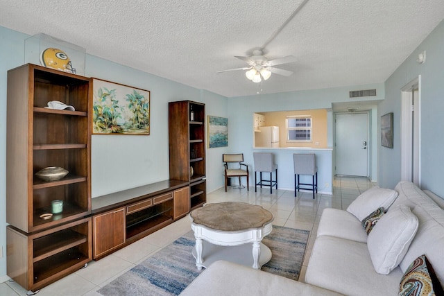 living room featuring a textured ceiling, light tile patterned flooring, visible vents, and ceiling fan