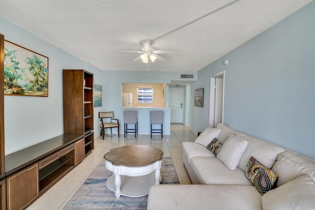 living area with light tile patterned floors, visible vents, a textured ceiling, and ceiling fan