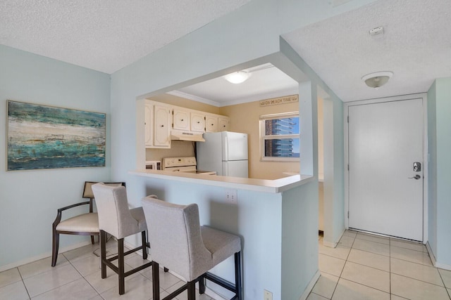 kitchen with under cabinet range hood, white appliances, a textured ceiling, and light tile patterned floors