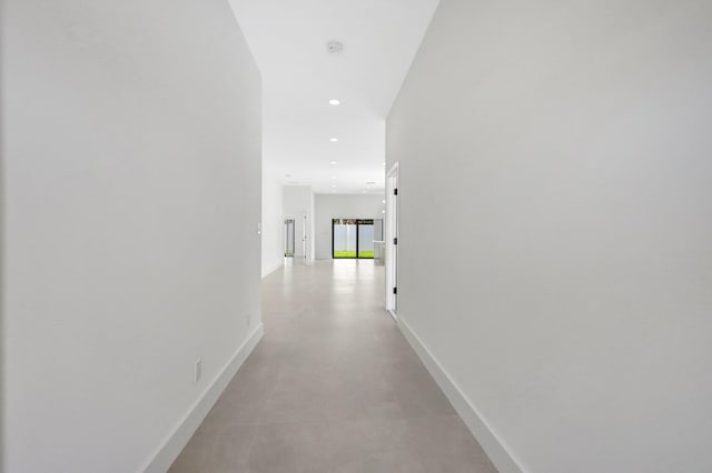 corridor with concrete flooring, recessed lighting, and baseboards