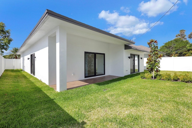 rear view of property with a fenced backyard, a yard, and stucco siding