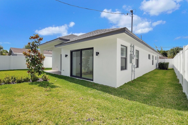 back of house featuring a shingled roof, a fenced backyard, a yard, and stucco siding