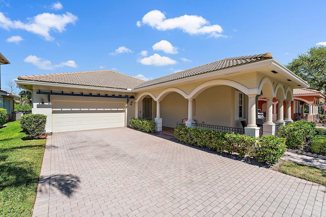 mediterranean / spanish-style home featuring stucco siding, a tiled roof, decorative driveway, and a garage