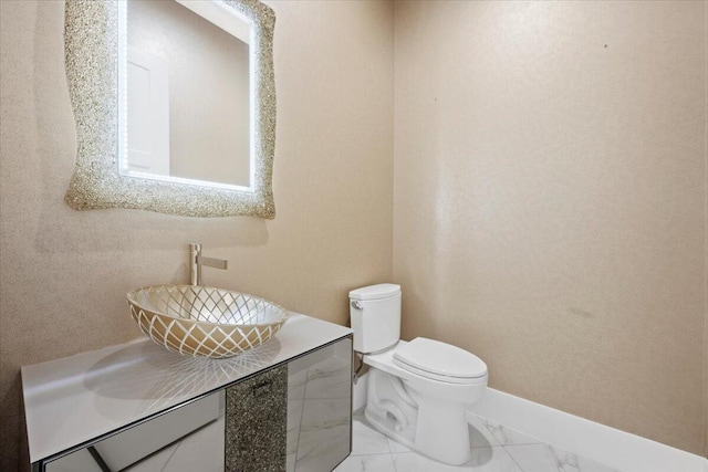 half bathroom featuring toilet, marble finish floor, baseboards, and a sink