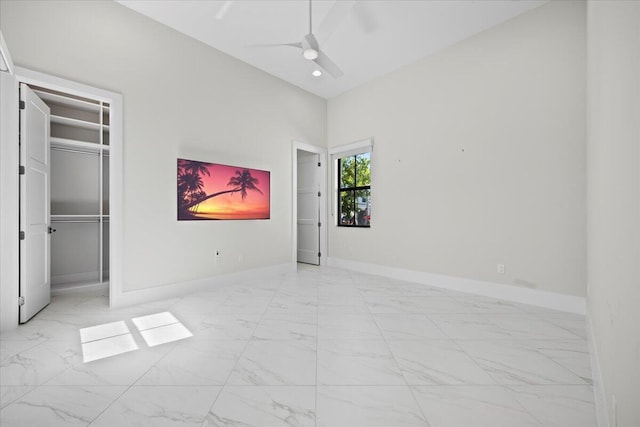 unfurnished bedroom featuring a walk in closet, marble finish floor, ceiling fan, high vaulted ceiling, and baseboards