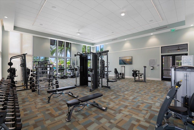 exercise room featuring a tray ceiling, carpet, visible vents, and baseboards