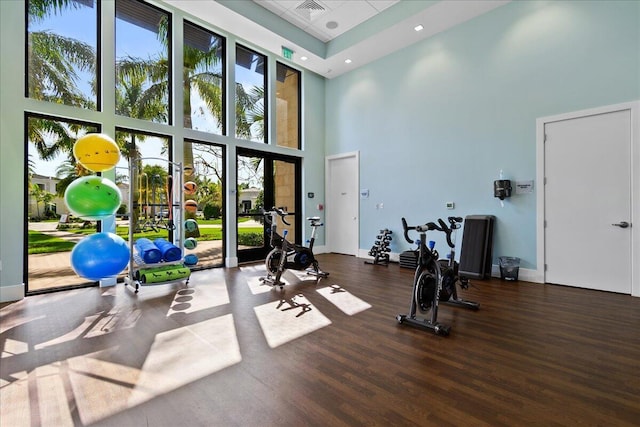 exercise room with a high ceiling, visible vents, baseboards, and wood finished floors