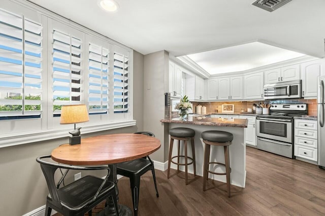 kitchen with white cabinets, stainless steel appliances, a peninsula, visible vents, and a breakfast bar