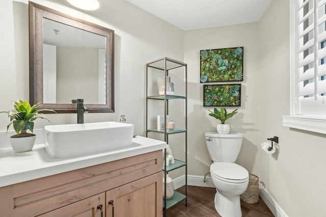 bathroom with toilet, vanity, baseboards, and wood finished floors