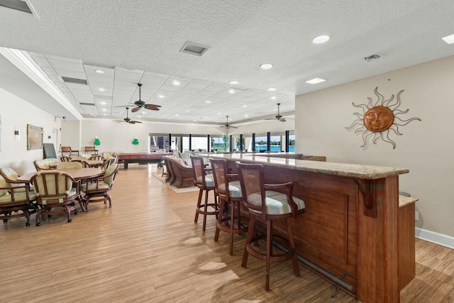 bar with visible vents, a dry bar, light wood-type flooring, and ceiling fan