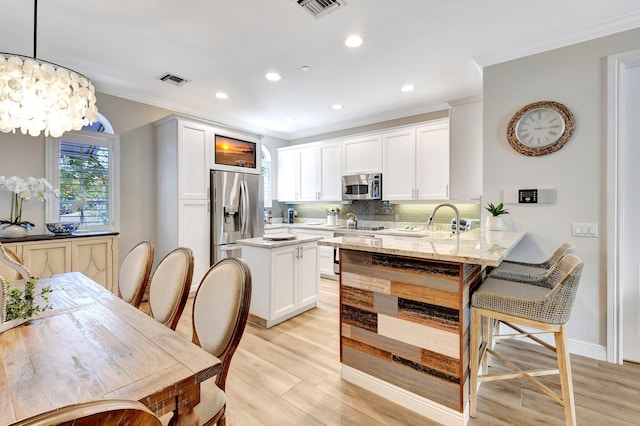 kitchen featuring tasteful backsplash, visible vents, appliances with stainless steel finishes, light wood-style floors, and ornamental molding