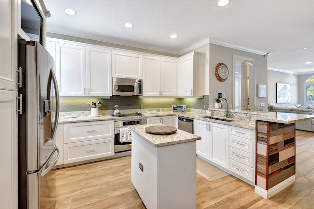 kitchen featuring light wood-style flooring, appliances with stainless steel finishes, open floor plan, a sink, and a peninsula