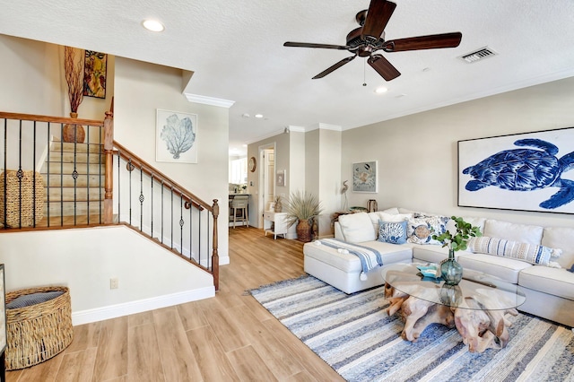 living area featuring wood finished floors, visible vents, baseboards, stairs, and crown molding