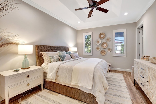 bedroom with baseboards, a raised ceiling, light wood-style flooring, crown molding, and recessed lighting