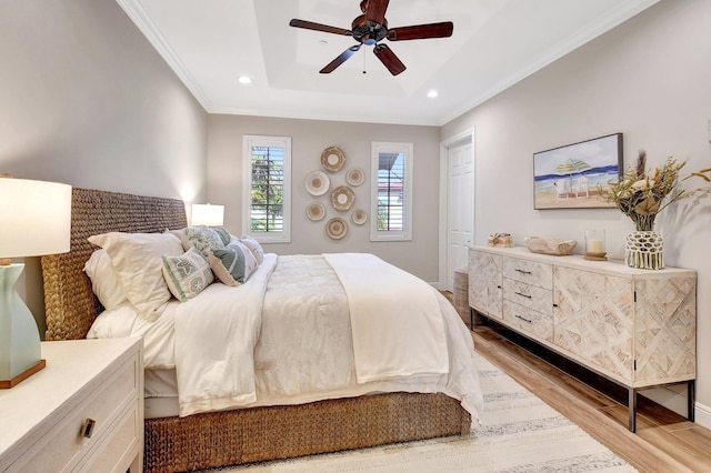 bedroom featuring baseboards, a raised ceiling, light wood-style flooring, ornamental molding, and recessed lighting