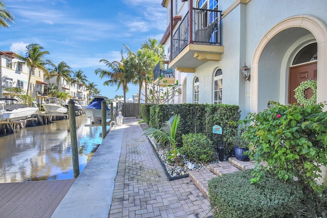 exterior space featuring a water view, boat lift, a balcony, and fence