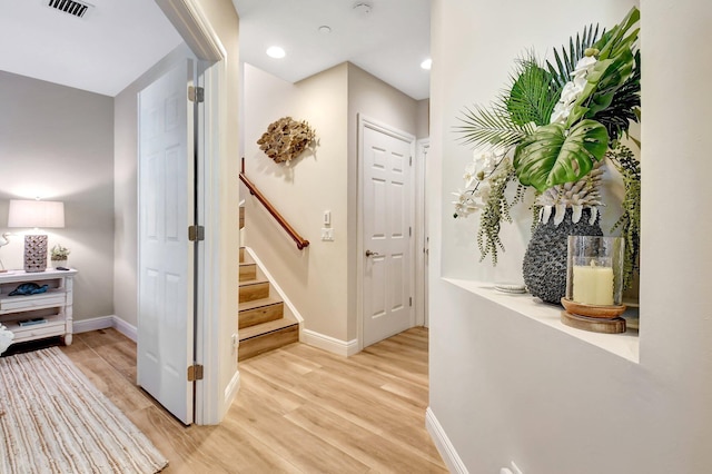 corridor featuring stairway, light wood-type flooring, visible vents, and baseboards