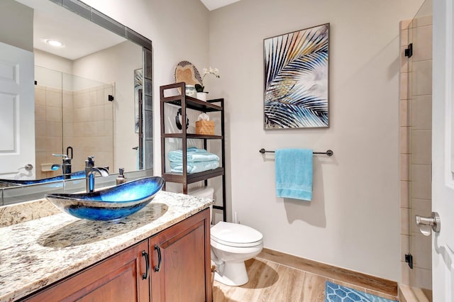 full bath featuring toilet, wood finished floors, vanity, baseboards, and a shower stall