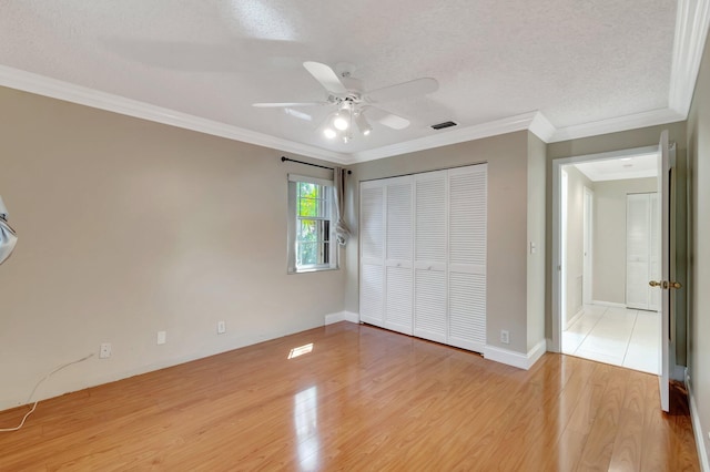 unfurnished bedroom with visible vents, crown molding, light wood-type flooring, a closet, and a textured ceiling