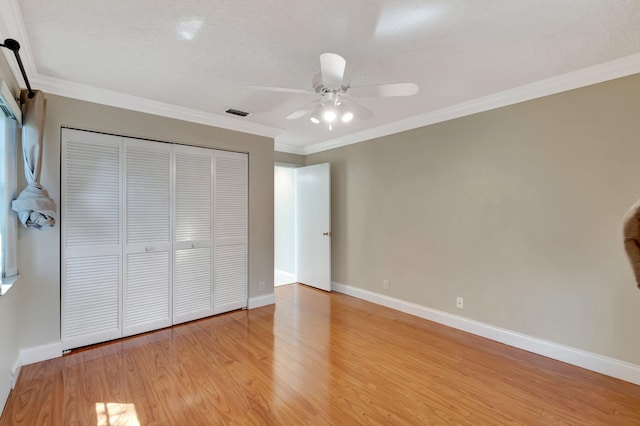 unfurnished bedroom featuring a closet, light wood-style flooring, crown molding, and baseboards