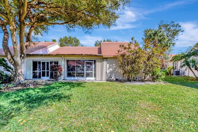 back of property featuring stucco siding, a tiled roof, central AC, and a yard