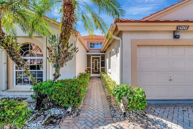 doorway to property with a tiled roof, a garage, and stucco siding