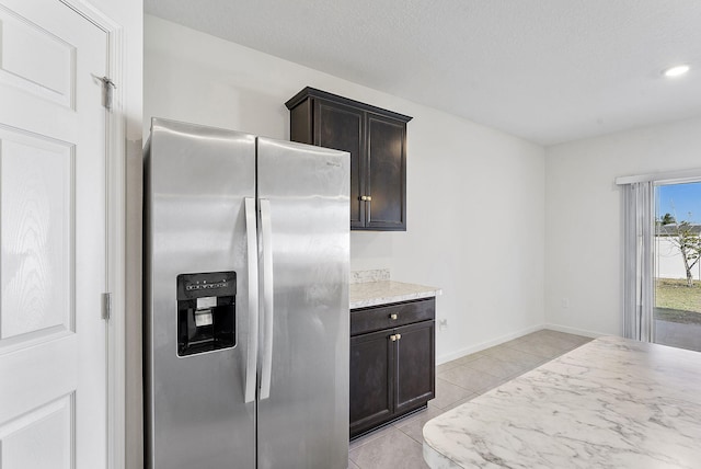 kitchen featuring light tile patterned floors, baseboards, dark brown cabinetry, stainless steel refrigerator with ice dispenser, and a textured ceiling