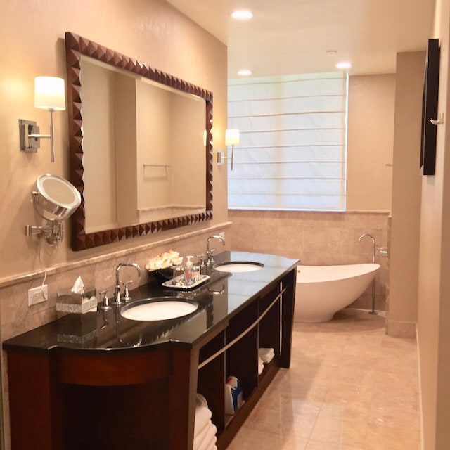 bathroom featuring double vanity, a freestanding tub, tile walls, and a sink