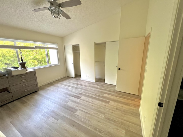 unfurnished bedroom featuring light wood finished floors, multiple closets, vaulted ceiling, a textured ceiling, and baseboards